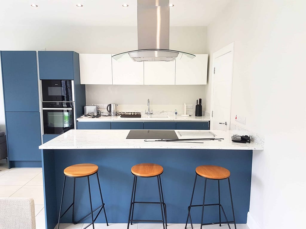 Vibrant blue kitchen cabinets with white marble countertops, modern appliances, and contemporary bar stools, showcasing professional interior painting services in Portstewart by G&E Interior Painting.