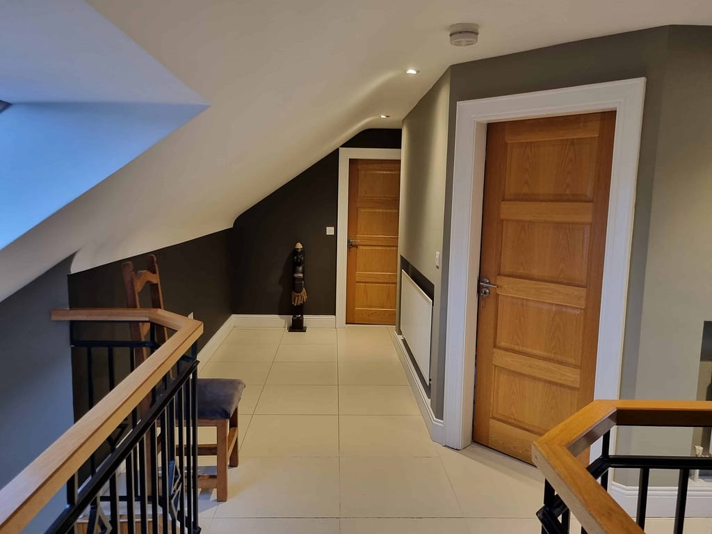 Brightly lit attic hallway with contemporary interior design, featuring wooden doors, a black and white color scheme, and stylish decor, perfectly painted by expert painters in Portstewart.