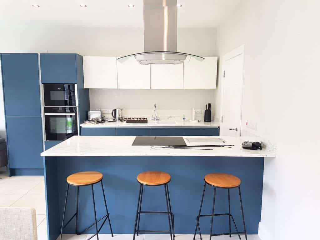 Vibrant blue kitchen cabinets with white marble countertops, modern appliances, and contemporary bar stools, showcasing professional interior painting services in Portstewart by G&E Interior Painting.
