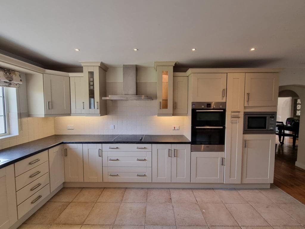 Bright white kitchen cabinets with modern stainless steel appliances and black countertops, showcasing professional interior painting services in Portstewart.