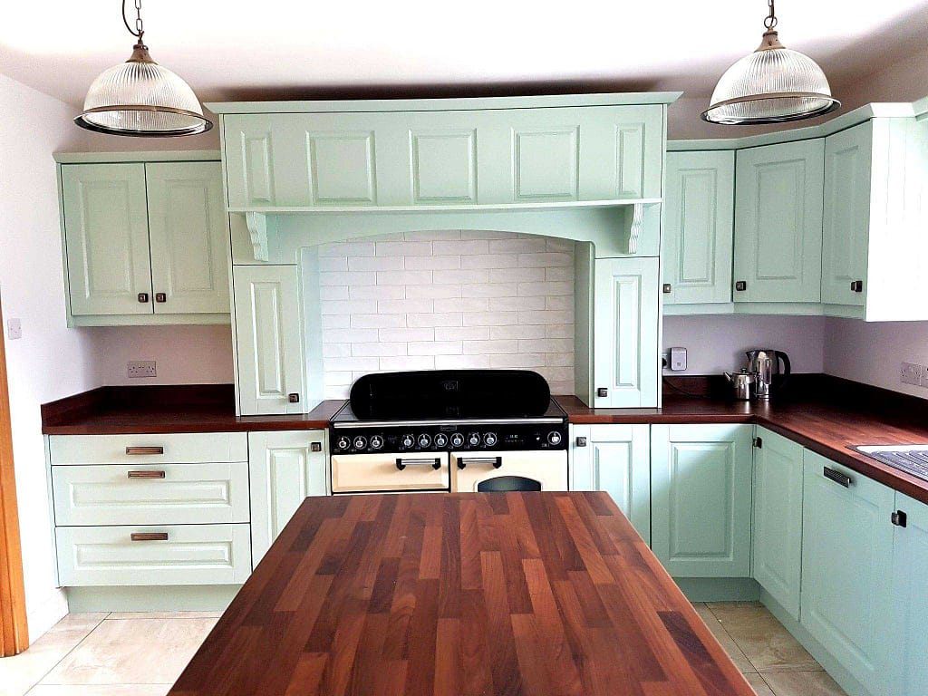 Bright pastel green kitchen cabinetry with wooden countertops and a black vintage-style stove, highlighting professional interior painting services in Portstewart for a refreshed home look.