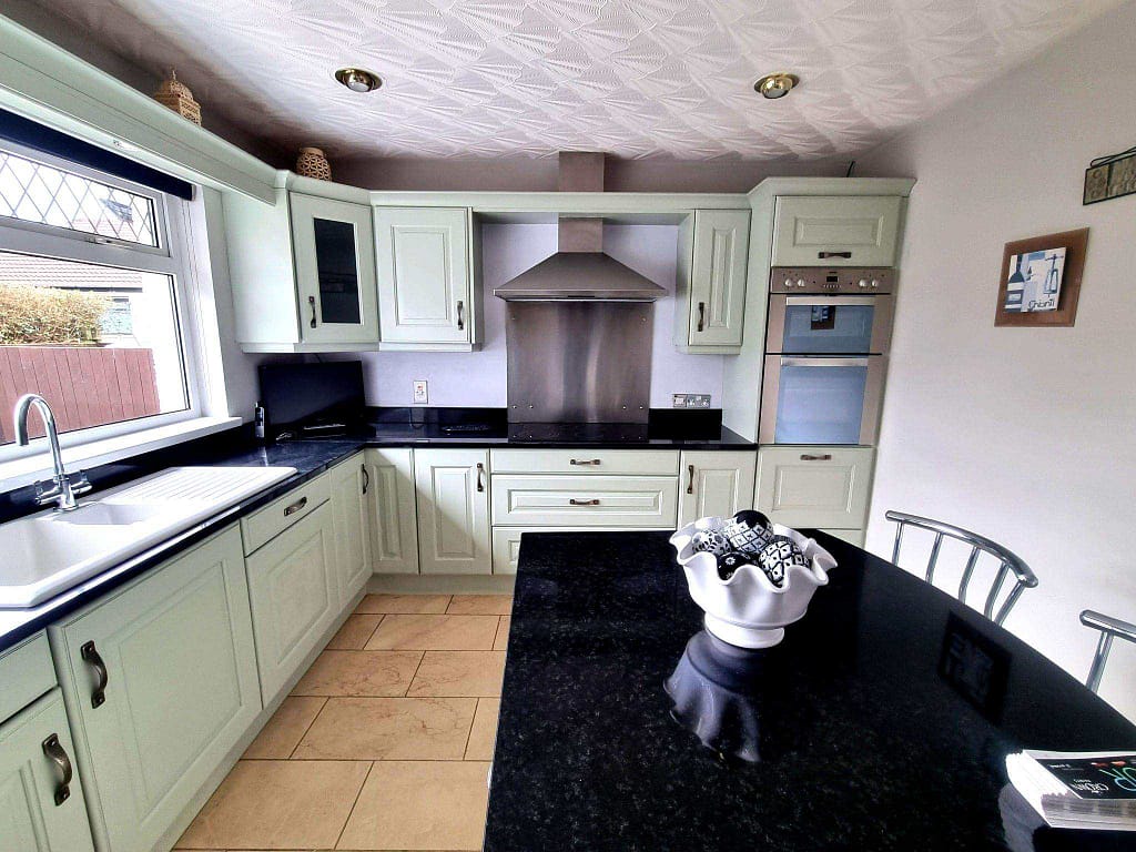 Bright white kitchen cabinets with black countertops, stainless steel appliances, and a large window providing natural light. Modern interior painting enhances the clean, stylish look of the home in Portstewart.