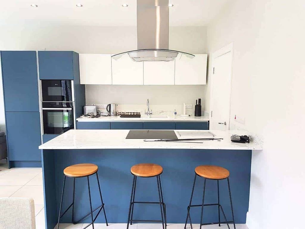 Modern kitchen interior with blue and white cabinetry, marble countertops, and wooden bar stools, showcasing expert interior painting services by G&E Interior Painting in Portstewart.