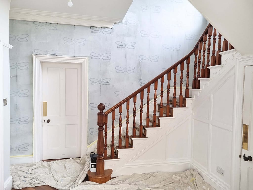 Smooth pale blue interior wall with butterfly pattern after painting renovation in Portstewart, featuring wooden staircase and white wainscoting.