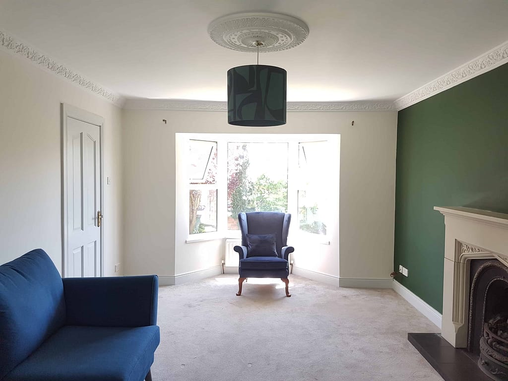 Bright living room interior painted by G&E Interior Painting in Portstewart, showcasing a fresh white wall with a contrasting green accent wall, elegant ceiling molding, and modern furnishings.
