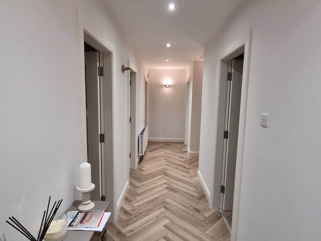 Modern interior hallway painted in neutral white shades with wood-effect flooring, showcasing professional interior painting services in Portstewart by G&E Interior Painting.