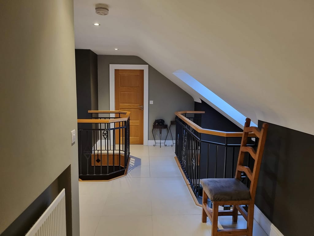 Interior hallway and landing with neutral painted walls, dark staircase balustrade and wooden handrail.