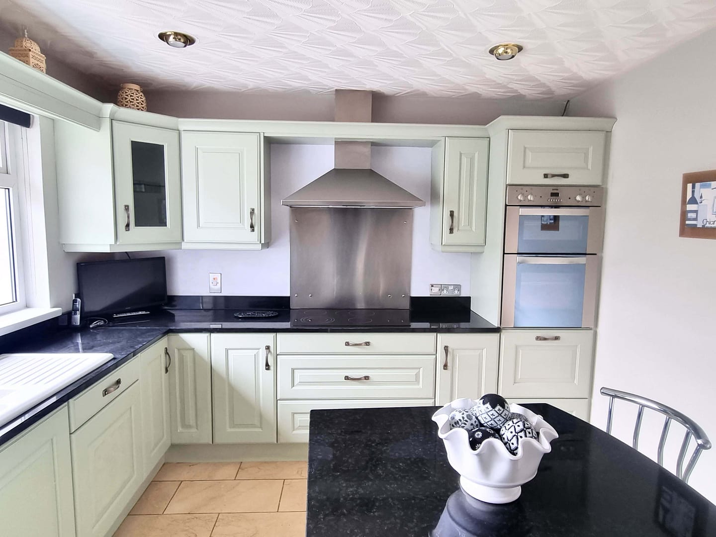 Modern kitchen with light green cabinets and island Kitchen with pale green painted cupboards, black worktops and stainless steel appliances.