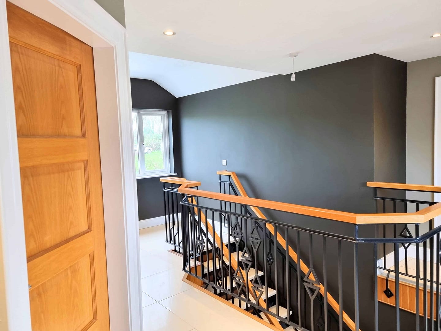 Modern home staircase with wooden railings in bushmills Modern upstairs landing with charcoal grey feature wall, wooden doors and black staircase balustrade.