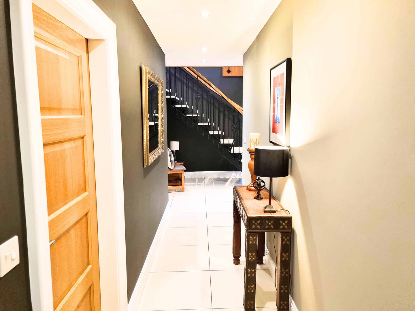 Contemporary hallway with elegant decor and staircase Bright sitting room with neutral painted walls, grey sofa, mustard yellow cushions and large window.