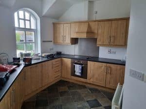 20240422_082322 Culinary kitchen with natural wooden cabinets, black countertops, kitchen appliances, and large arched window in Portstewart, showcasing expert interior painting services.