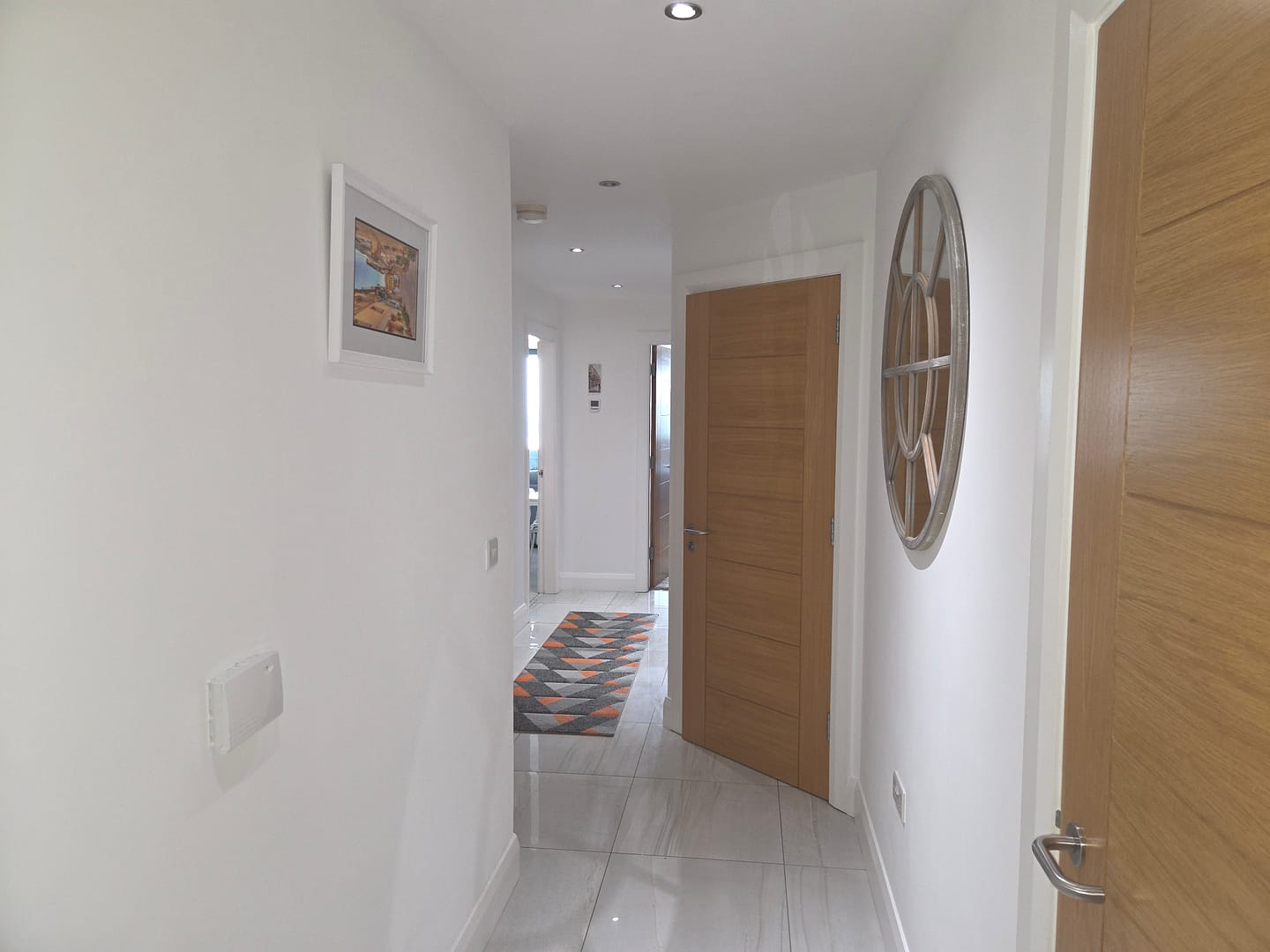 Interior hallway with freshly painted white walls, white ceiling, natural wood doors and light tiled flooring.